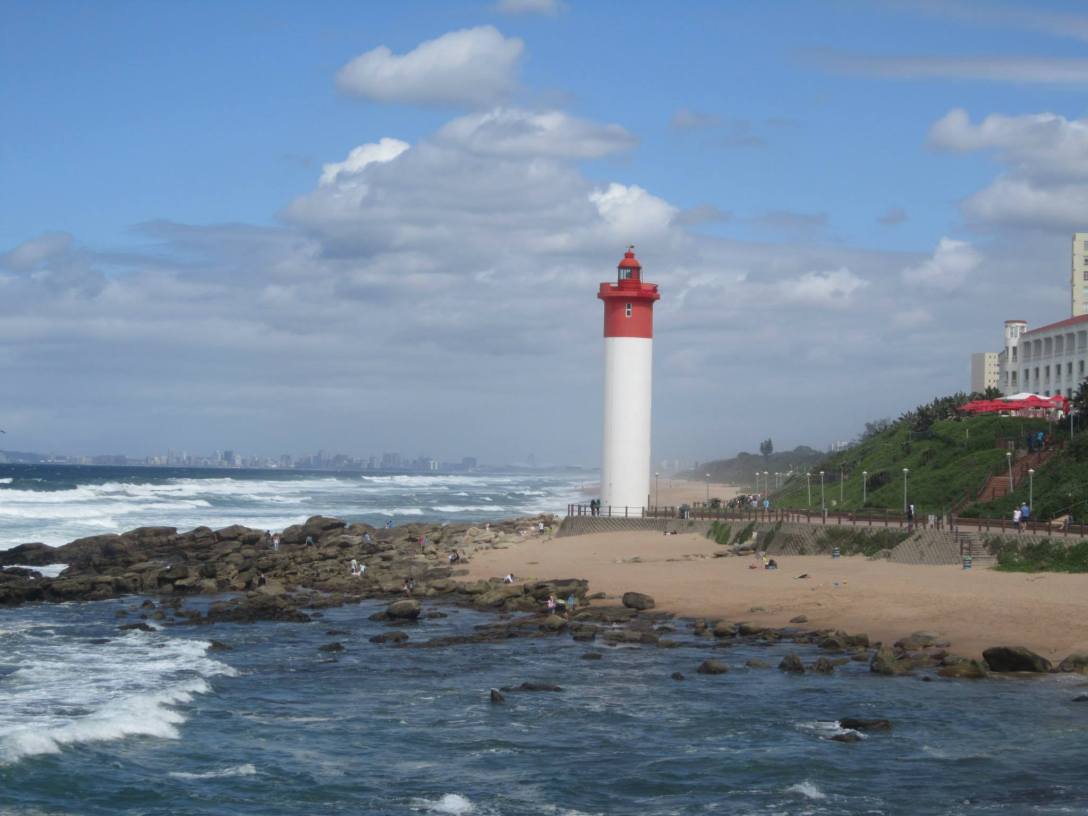 Red and white lighthouse standing on the South African coastline with waves crashing on the rocks below, photographed in Durban, South Africa, 2014