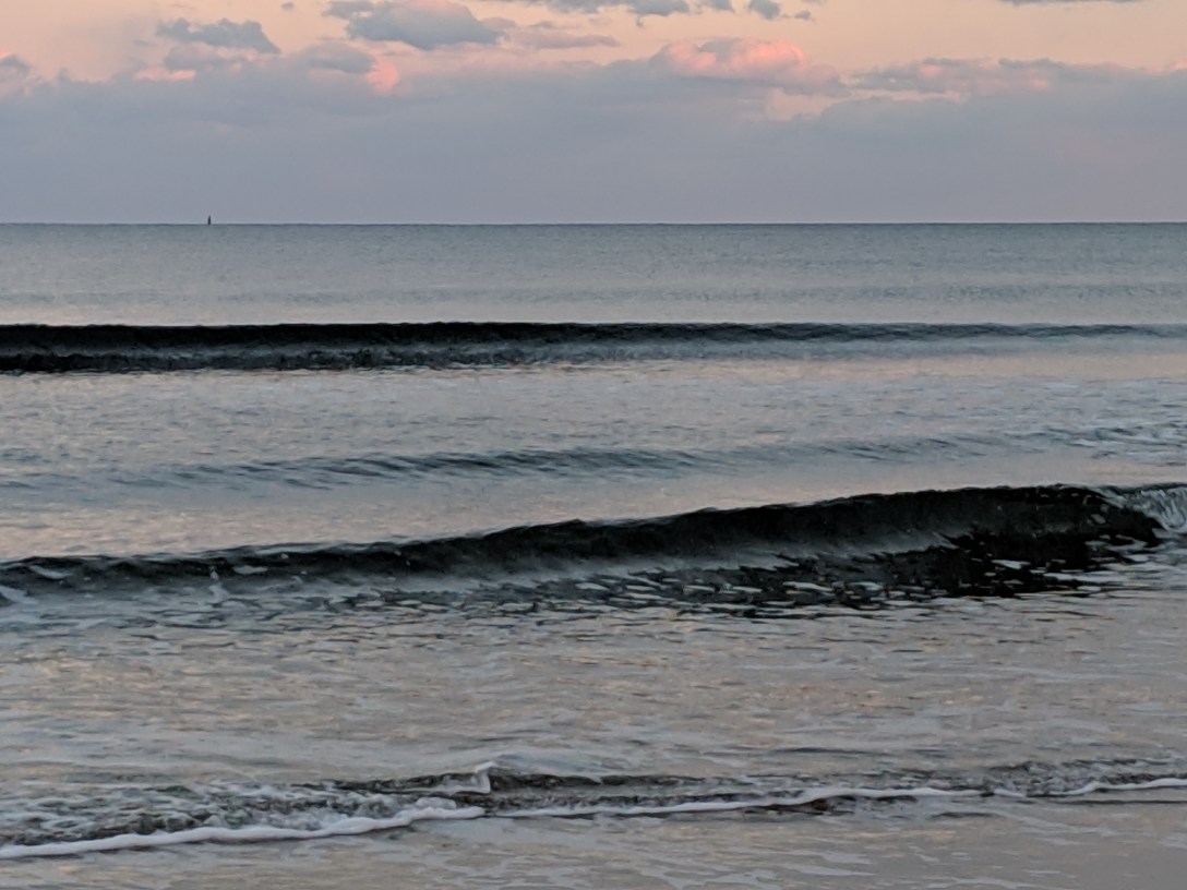 A gentle ocean wave gathering before it breaks, captured at dusk with muted grey-blue tones