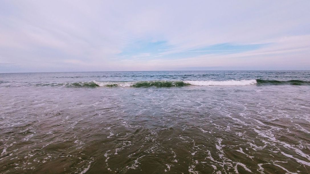 A single wave breaking across a calm blue-grey sea beneath a soft overcast sky at Hampton Beach.